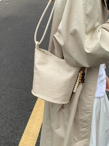 Fashionable beige woven bucket bag with tassel detail styled on a street model