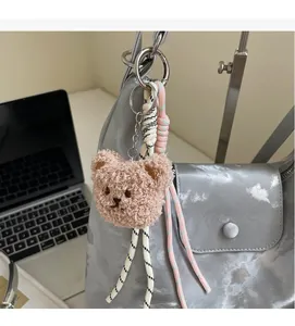 Close-up of a pink plush bear keychain with woven cord on a grey tote bag detail