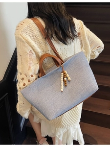Blue canvas tote bag with brown leather straps and beaded charm on model