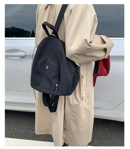Detail view of a black multi-functional backpack worn by a model in a beige coat