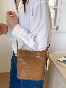 Brown woven bucket bag with crossbody strap and wooden bead charm for summer style