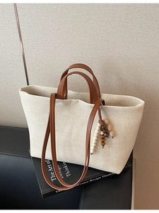 Minimalist beige canvas tote bag with brown faux leather straps on a sofa