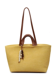 Bright yellow woven tote bag with brown leather handles and wooden bead charm decor