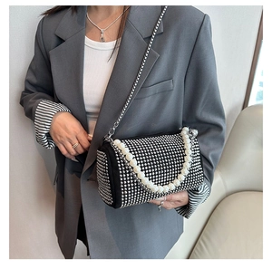 Detail of black Boston bag featuring silver studs, pearl handle, and metal chain strap