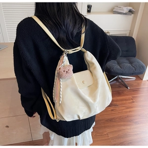 Detail of a creamy white crescent backpack with a cute brown bear charm and colorful tassel