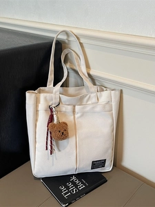 Minimalist beige canvas tote bag with large front pocket and plush bear pendant