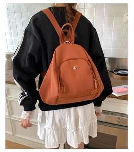 Detail of orange nylon backpack showing wide straps and curved zip pocket on the front