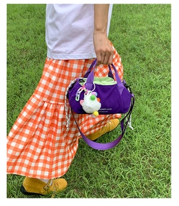 Detail of purple nylon crossbody bag with white plush ball and drawstring closure
