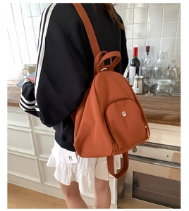 Close-up of caramel brown nylon backpack with round metal logo and zip pocket detail