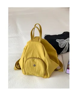 Detail of a bright yellow mini nylon backpack featuring sleek silver metal logo hardware