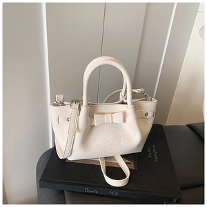 Dettaglio borsa in pelle litchi color crema con fiocco elegante e tracolla sottile