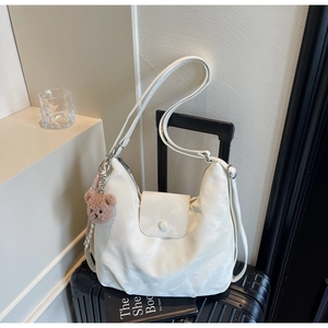 Detail of cream white tote bag with front pocket and plush bear charm on a suitcase