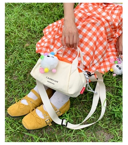 Detail of cream canvas tote bag featuring plush charm and shoulder strap on grass