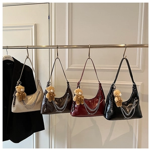 Detailansicht der glänzenden Hobo-Taschen aus Lackleder mit Ketten und Bären-Anhänger