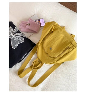 Detail of yellow nylon backpack featuring round zipper pocket and metallic logo emblem