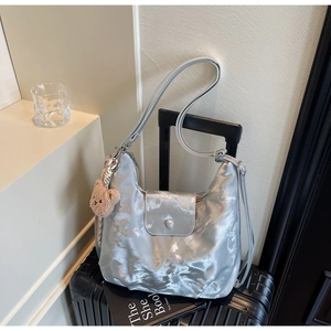 Silver satin hobo tote bag with teddy bear charm placed on a black suitcase