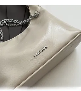 Detail der weichen cremefarbenen Ledertextur mit silbernem Logo und Kettenriemen der Tasche