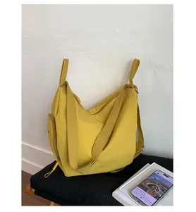 Detail of a bright yellow nylon tote bag with wide strap and side zip pocket on black padding