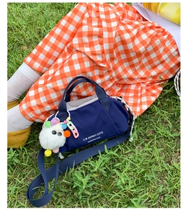 Detail of navy canvas bucket bag with plush charm and chain strap on outdoor grass