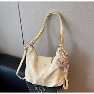 Detail of cream faux leather shoulder bag with soft texture and cute brown plush bear charm