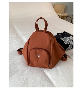 Detail view of rust-red multi-functional backpack on white bed with fabric texture and logo