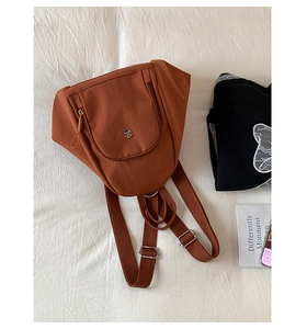 Detailed close-up of brown nylon backpack with round metal logo and zip pocket