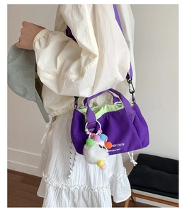 Detail of purple canvas crossbody bag with drawstring closure and plush monster charm