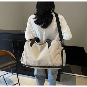 Detail view of cream travel bag featuring a reinforced handle and bottom shoe compartment