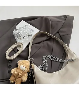 Detail der cremeweißen Halbmondtasche mit Silberkette und süßem Teddybär-Anhänger