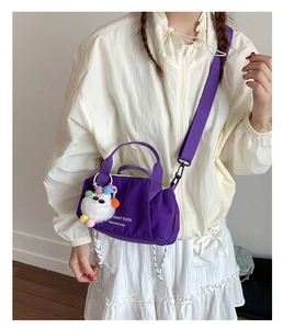 Detailed close-up of dark purple nylon crossbody bag featuring stylish white text and furry charm