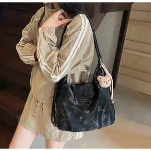 Detail of black large capacity shoulder bag with cute plush bear charm on a female model