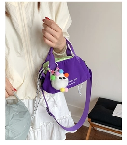 Detail of purple canvas crossbody bag featuring a plush monster charm and colorful pom-poms
