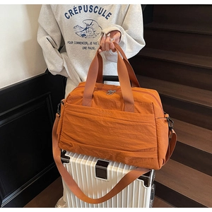 Détail macro du sac de voyage en nylon orange posé sur une valise en tissu indéchirable