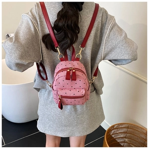 Detail of pink mini backpack with black heart print and red straps worn by a model