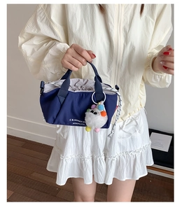 Detail of navy canvas tote bag featuring gray drawstring closure and a colorful pom pom charm