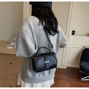 Detail of black leather square bag with silver H-buckle worn by a model in lifestyle setting