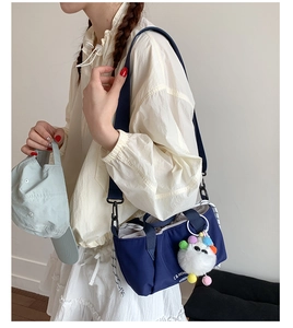 Detail of navy nylon shoulder bag with cute monster plush charm shown by a model
