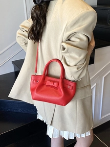Borsa a secchiello rossa in pelle martellata con fiocco indossata su abito beige