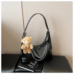 Detail einer schwarzen Halbmond-Schultertasche mit Silberketten und kleinem Plüschbären