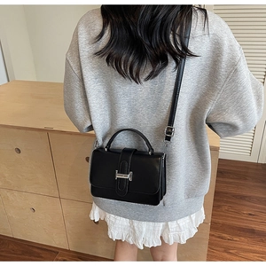 Detail view of black square crossbody bag with silver H-shaped buckle on an elegant model