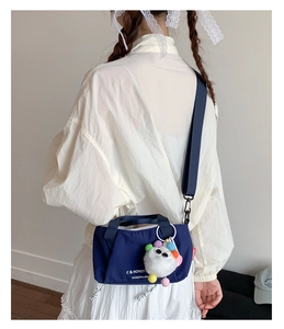 Detail of navy canvas crossbody bag with white text print and a cute plush toy charm