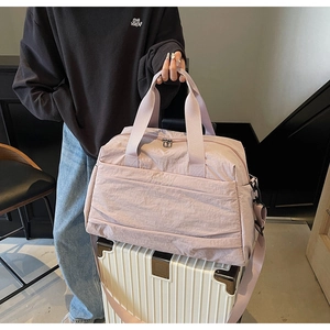 Sac de voyage rose avec bandoulière posé sur une valise blanche à rayures