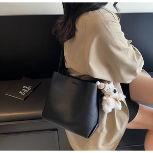 Detail of a black leather bucket bag featuring a cute plush puppy charm accessory