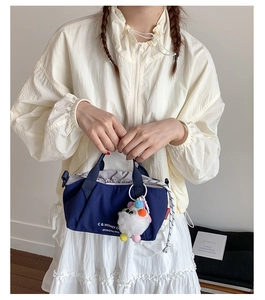 Close-up of navy canvas bag featuring white typography and a white plush pompom charm