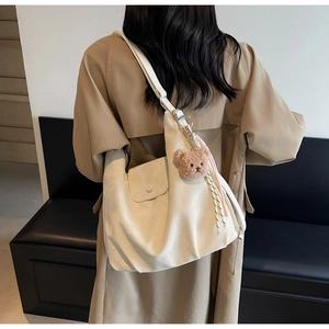 Detail view of cream crossbody dumpling bag with cute plush bear charm on a trench coat