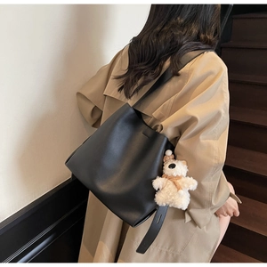 Minimalist black bucket bag with plush bear charm worn by model on a wide shoulder strap