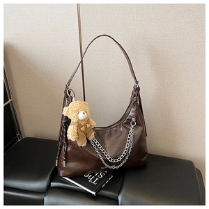 Nahaufnahme einer braunen Lackleder-Hobo-Tasche mit Ketten und Bärenanhänger