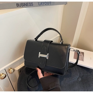 Close-up of black crossbody bag featuring a silver H-shaped buckle on smooth leather