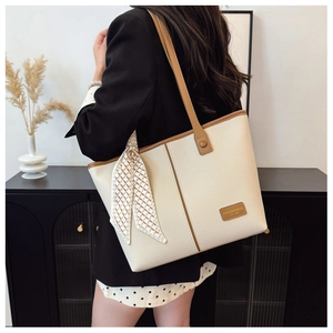Detail of minimalist cream tote bag featuring brown trim and elegant silk scarf on handle