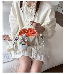 Detail view of cream canvas bucket bag with orange drawstring and cute plush monster charm